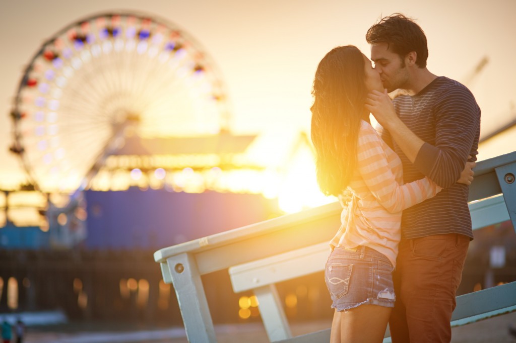 romantic couple kissing at sunset in front of santa monica ferris wheel.